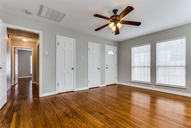 unfurnished bedroom featuring ceiling fan, dark wood-type flooring, and multiple closets