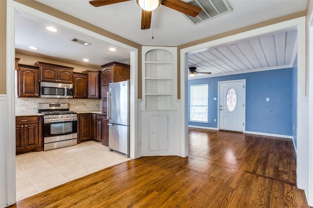 kitchen featuring appliances with stainless steel finishes, built in features, decorative backsplash, ceiling fan, and light wood-type flooring