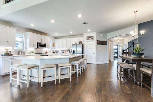 kitchen featuring pendant lighting, stainless steel appliances, a center island with sink, and white cabinets