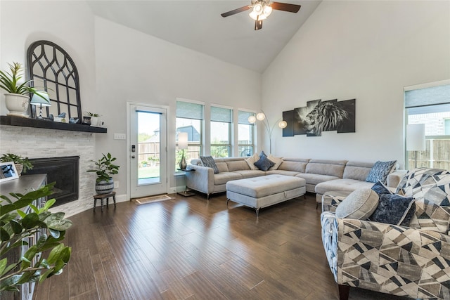 living room featuring dark hardwood / wood-style floors, high vaulted ceiling, a stone fireplace, and a wealth of natural light