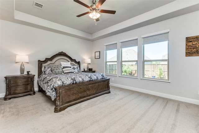 carpeted bedroom featuring ceiling fan and a tray ceiling