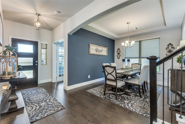 dining room featuring dark wood-type flooring, a raised ceiling, and a notable chandelier