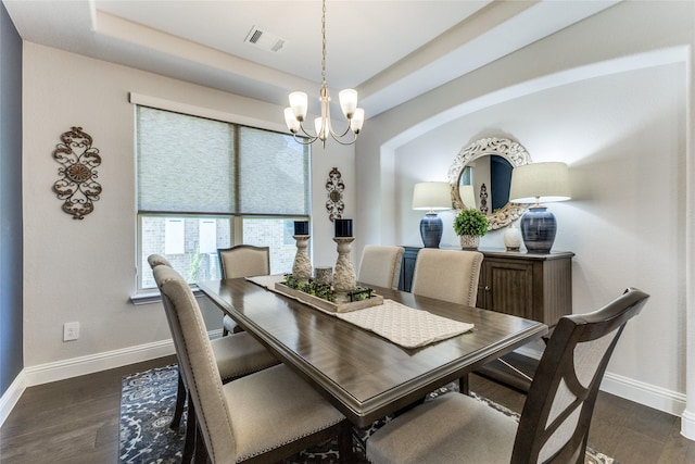 dining area featuring an inviting chandelier, a tray ceiling, and dark wood-type flooring