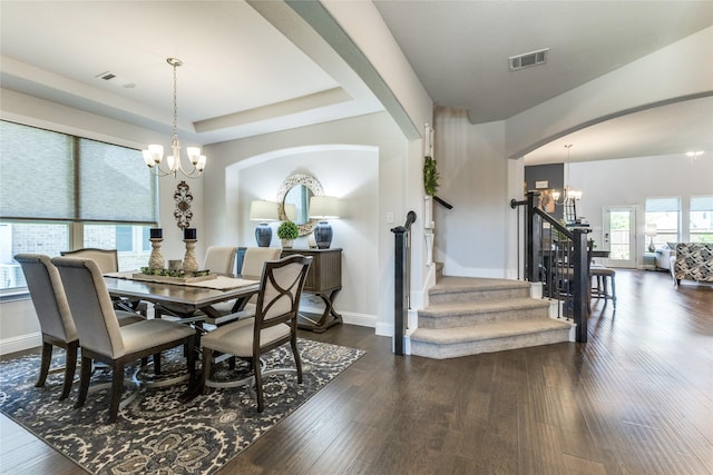 dining space featuring a tray ceiling, dark hardwood / wood-style flooring, and a notable chandelier