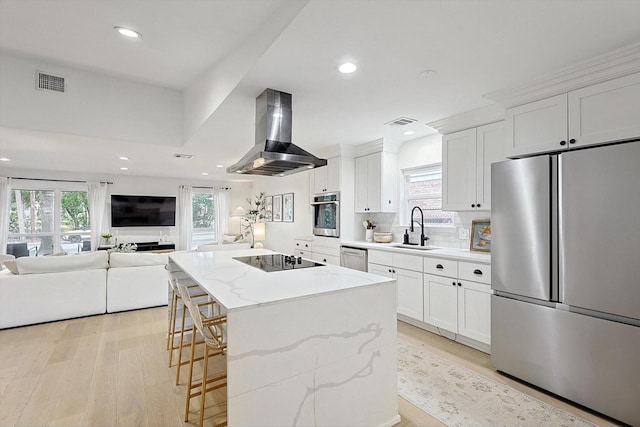 kitchen with sink, stainless steel appliances, island exhaust hood, white cabinets, and a kitchen island