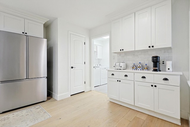 kitchen with white cabinets, light hardwood / wood-style floors, stainless steel refrigerator, and washing machine and clothes dryer