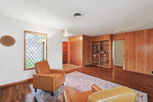 living area featuring built in shelves, wooden walls, and wood-type flooring