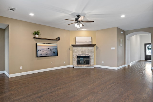 unfurnished living room featuring arched walkways, a fireplace, dark wood finished floors, a ceiling fan, and baseboards