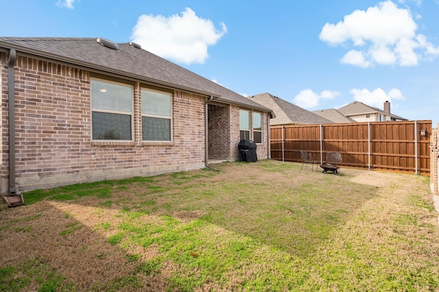 back of house with a yard, an outdoor fire pit, fence, and brick siding