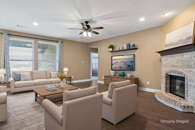 living room featuring visible vents, ceiling fan, a stone fireplace, wood finished floors, and baseboards