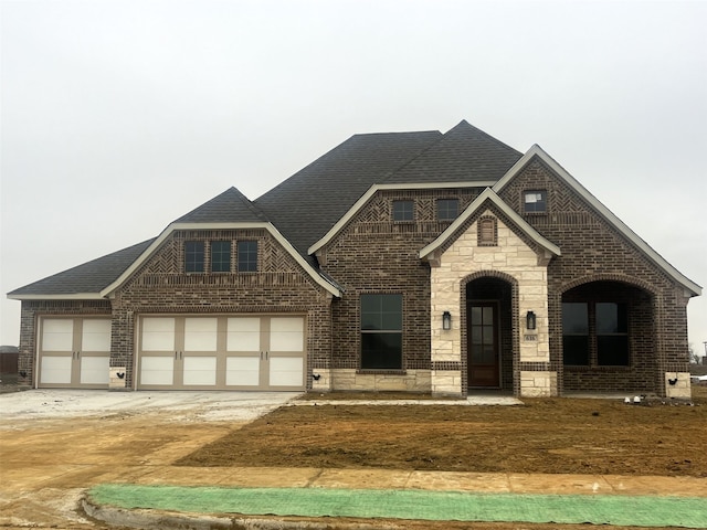 view of front of home featuring an attached garage, brick siding, driveway, stone siding, and roof with shingles