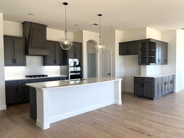 kitchen with arched walkways, black stovetop, visible vents, stainless steel oven, and premium range hood