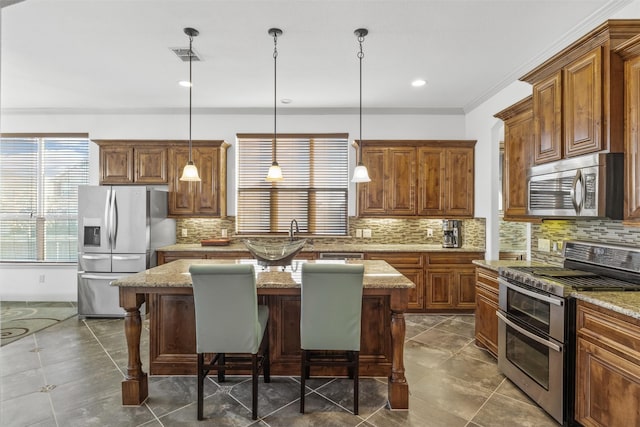 kitchen with decorative light fixtures, appliances with stainless steel finishes, a kitchen breakfast bar, a kitchen island, and light stone countertops