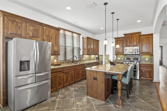 kitchen with a kitchen bar, light stone counters, a kitchen island, pendant lighting, and stainless steel appliances