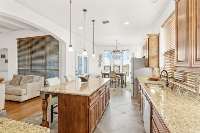 kitchen featuring a kitchen island, a breakfast bar, decorative light fixtures, sink, and light stone counters