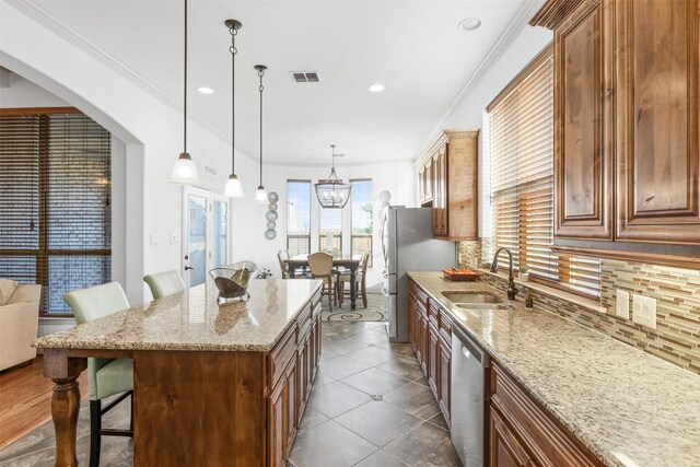 kitchen with sink, a breakfast bar area, hanging light fixtures, appliances with stainless steel finishes, and light stone countertops