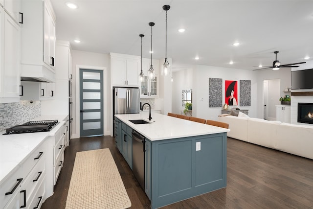 kitchen with appliances with stainless steel finishes, pendant lighting, sink, white cabinets, and a large island with sink