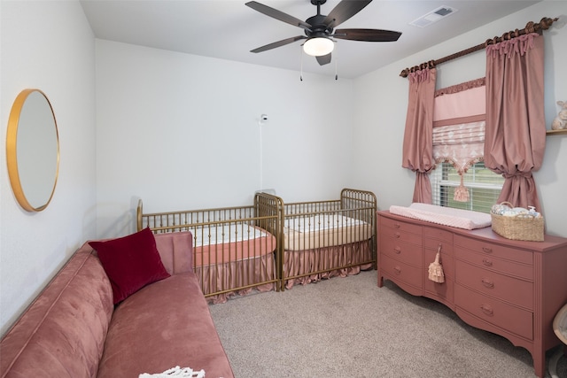 carpeted bedroom featuring a nursery area and ceiling fan
