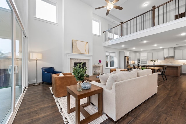 living room with ceiling fan, dark hardwood / wood-style floors, a tiled fireplace, and a high ceiling