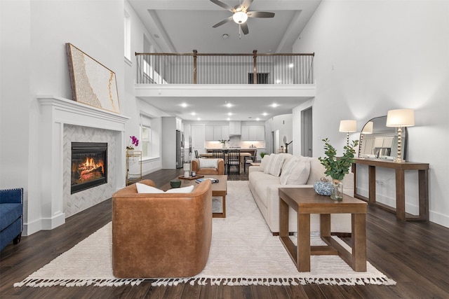 living room featuring a tiled fireplace, a high ceiling, dark wood-type flooring, and ceiling fan