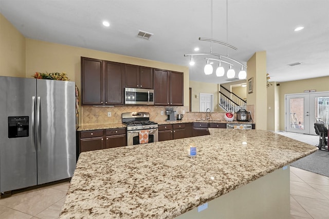 kitchen with light tile patterned floors, stainless steel appliances, dark brown cabinetry, decorative backsplash, and decorative light fixtures