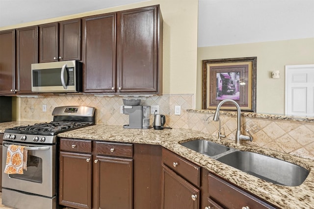 kitchen featuring sink, decorative backsplash, dark brown cabinetry, light stone counters, and stainless steel appliances