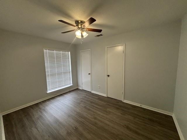 unfurnished bedroom featuring ceiling fan, dark wood-type flooring, and multiple closets