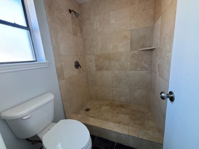 bathroom with tile patterned flooring, a tile shower, and toilet