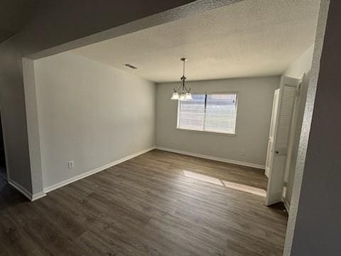 unfurnished dining area with dark wood-type flooring, a textured ceiling, and a notable chandelier