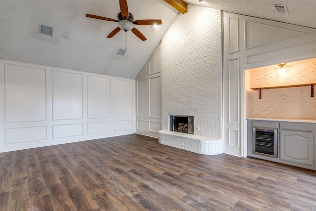 unfurnished living room featuring a brick fireplace, beam ceiling, hardwood / wood-style floors, and a textured ceiling