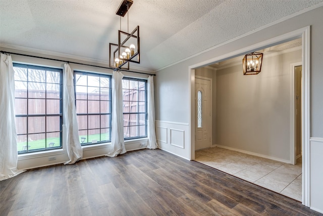 unfurnished dining area with an inviting chandelier, ornamental molding, wood-type flooring, and a textured ceiling