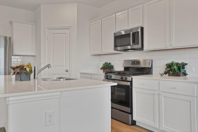 kitchen with white cabinetry, sink, stainless steel appliances, and a center island with sink