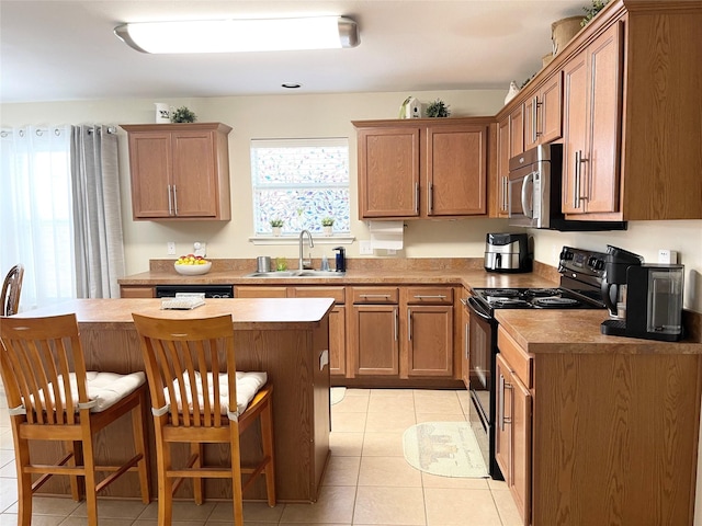 kitchen featuring sink, light tile patterned floors, a breakfast bar, black appliances, and a kitchen island