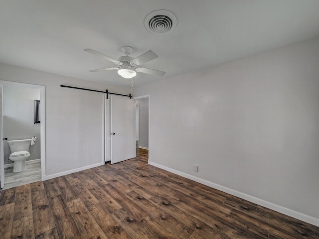 unfurnished bedroom featuring ceiling fan, a barn door, connected bathroom, and dark hardwood / wood-style flooring