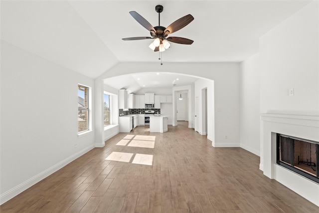 unfurnished living room with light wood-style floors, vaulted ceiling, a fireplace, and a ceiling fan