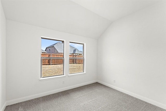 empty room featuring plenty of natural light, baseboards, vaulted ceiling, and carpet flooring