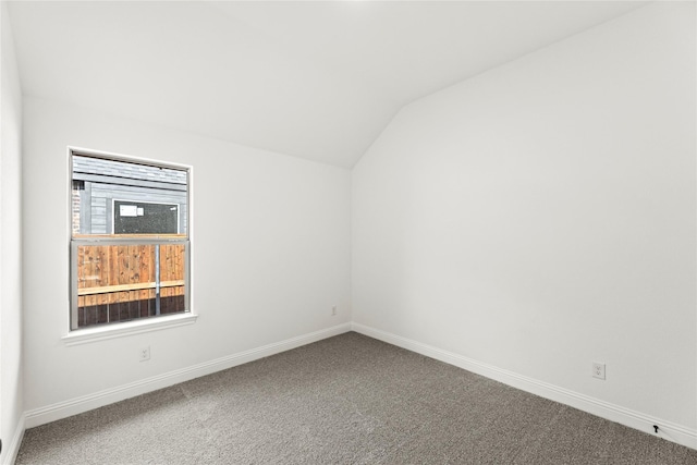 carpeted empty room featuring baseboards and vaulted ceiling