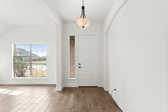 foyer featuring baseboards, arched walkways, and wood finished floors