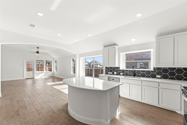 kitchen featuring visible vents, a sink, vaulted ceiling, light countertops, and backsplash