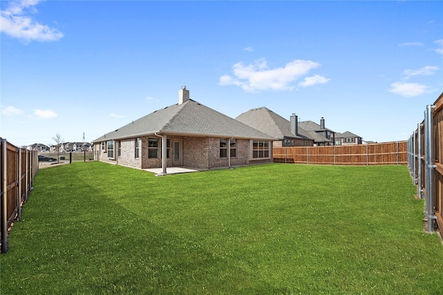 rear view of property featuring a patio area, brick siding, a lawn, and a fenced backyard