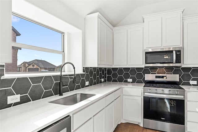 kitchen featuring light countertops, decorative backsplash, appliances with stainless steel finishes, white cabinets, and a sink