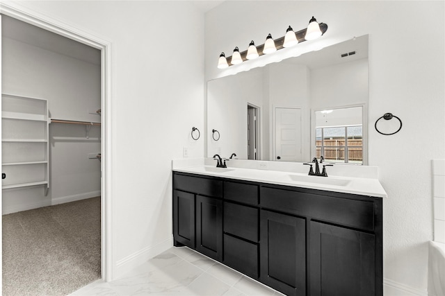 full bath featuring a sink, baseboards, marble finish floor, a spacious closet, and double vanity