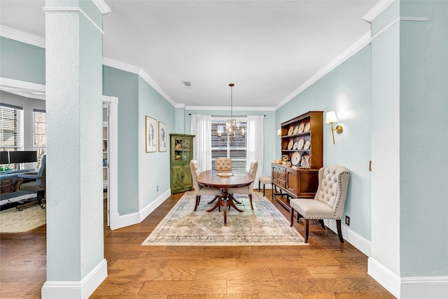 dining space featuring hardwood / wood-style floors, crown molding, a notable chandelier, and ornate columns