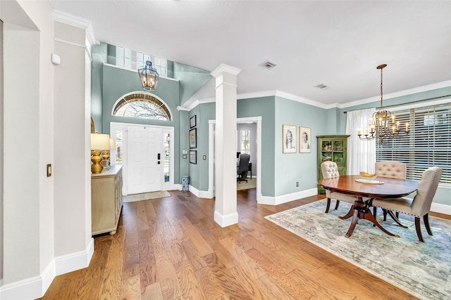 foyer featuring crown molding, hardwood / wood-style flooring, a chandelier, and ornate columns