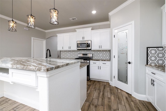 kitchen featuring stainless steel appliances, white cabinetry, light stone countertops, and an island with sink