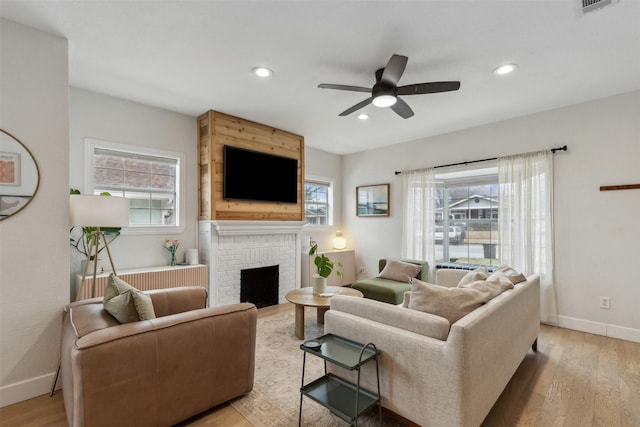 living room with a fireplace, ceiling fan, and light wood-type flooring