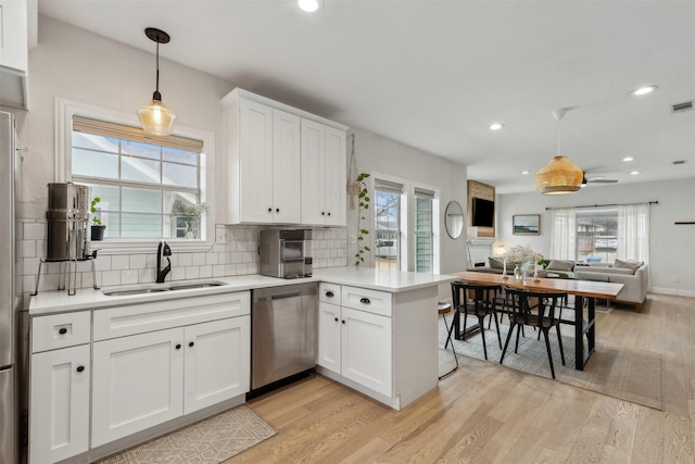 kitchen with sink, white cabinets, hanging light fixtures, stainless steel dishwasher, and kitchen peninsula