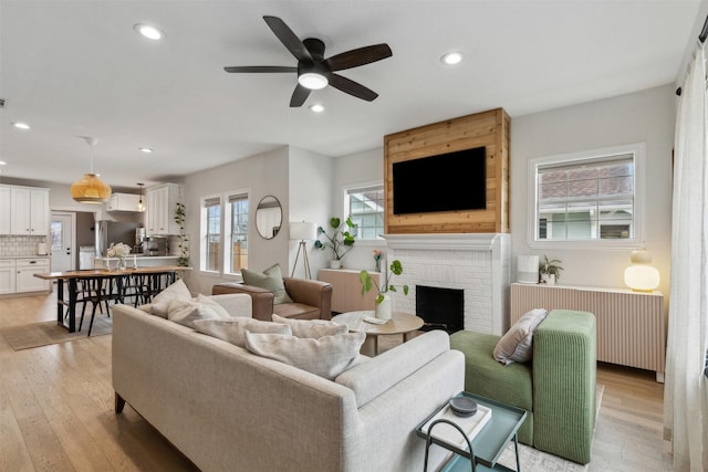 living room featuring ceiling fan, a fireplace, radiator, and light wood-type flooring