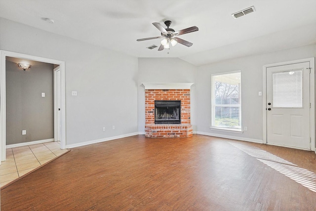 unfurnished living room featuring lofted ceiling, a brick fireplace, light hardwood / wood-style flooring, and ceiling fan