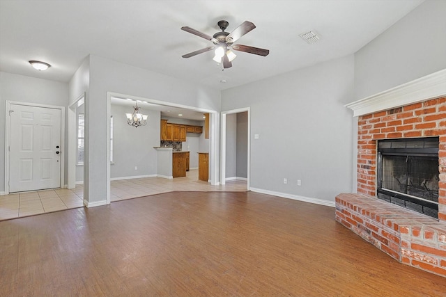 unfurnished living room with ceiling fan with notable chandelier, light hardwood / wood-style floors, and a brick fireplace